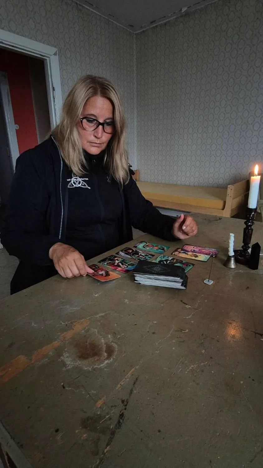 En kvinne legger tarotkort på et slitt bord i et tomt rom, med et tent stearinlys ved siden av