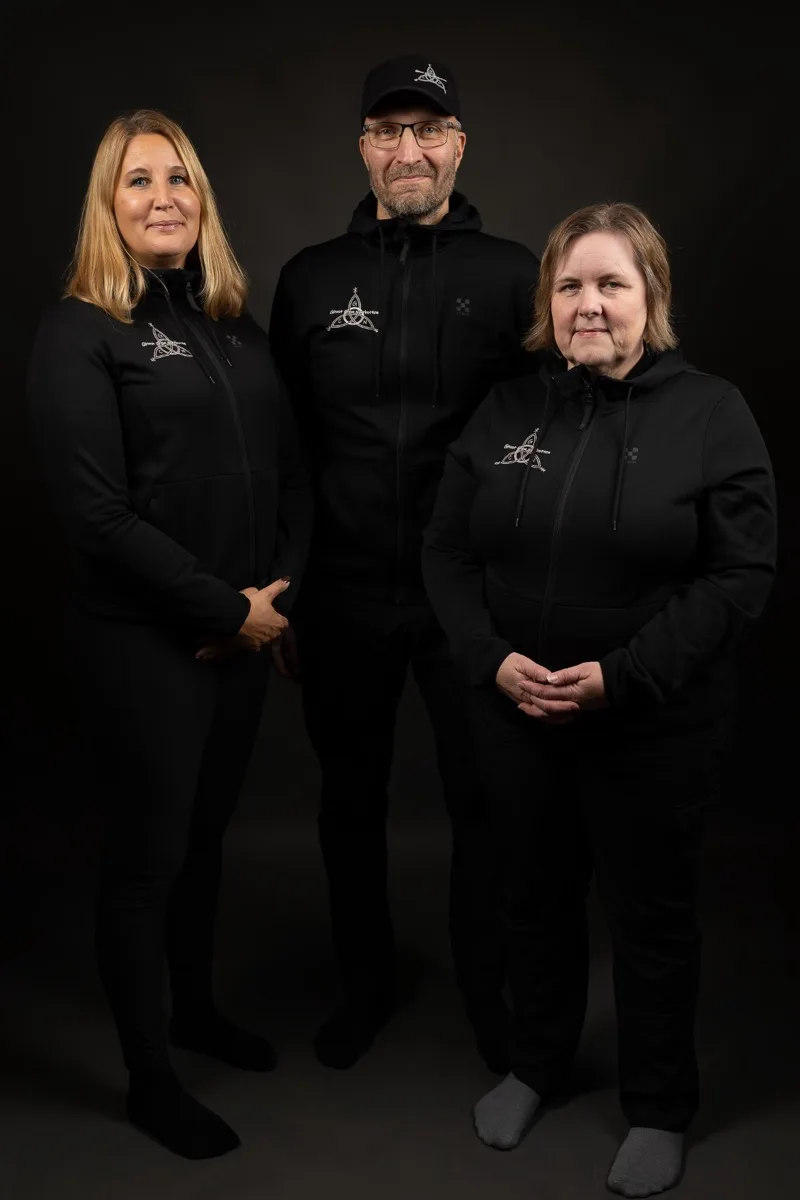 Tre personer i svarte gensere med Ghost Crew Norrbottens logo, fotografert mot svart bakgrunn