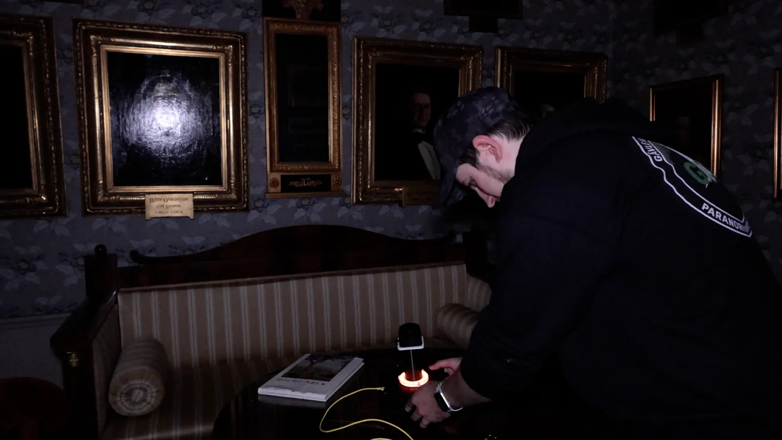 Joen setting up equipment on a table in front of a wall of gilt-framed portraits
