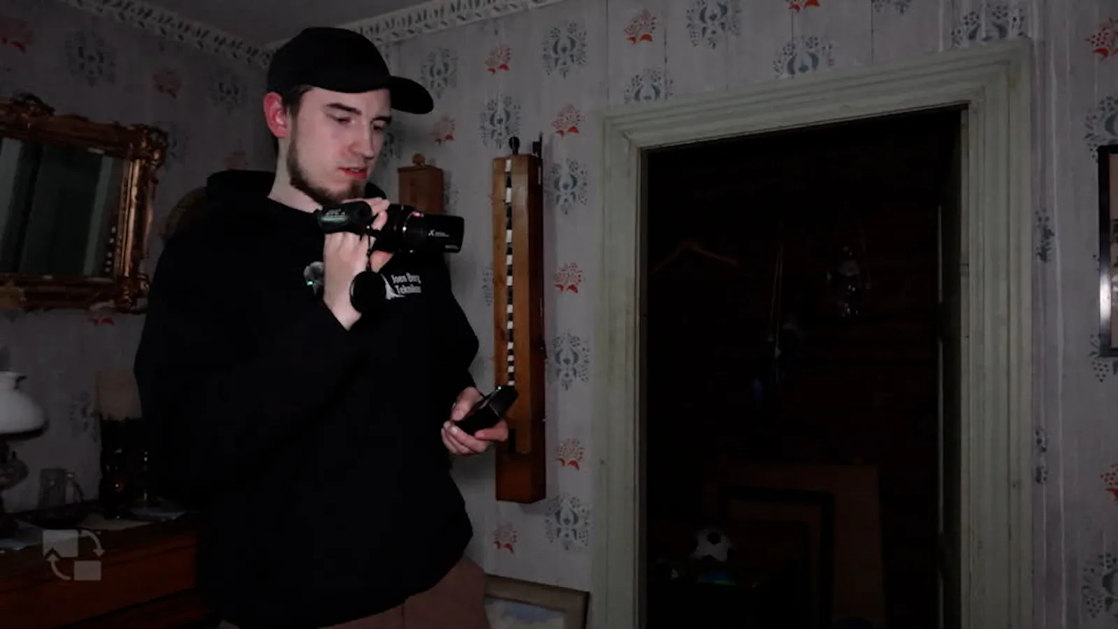 Joen filming with a handheld camera in a floral-wallpapered room at Frammegården