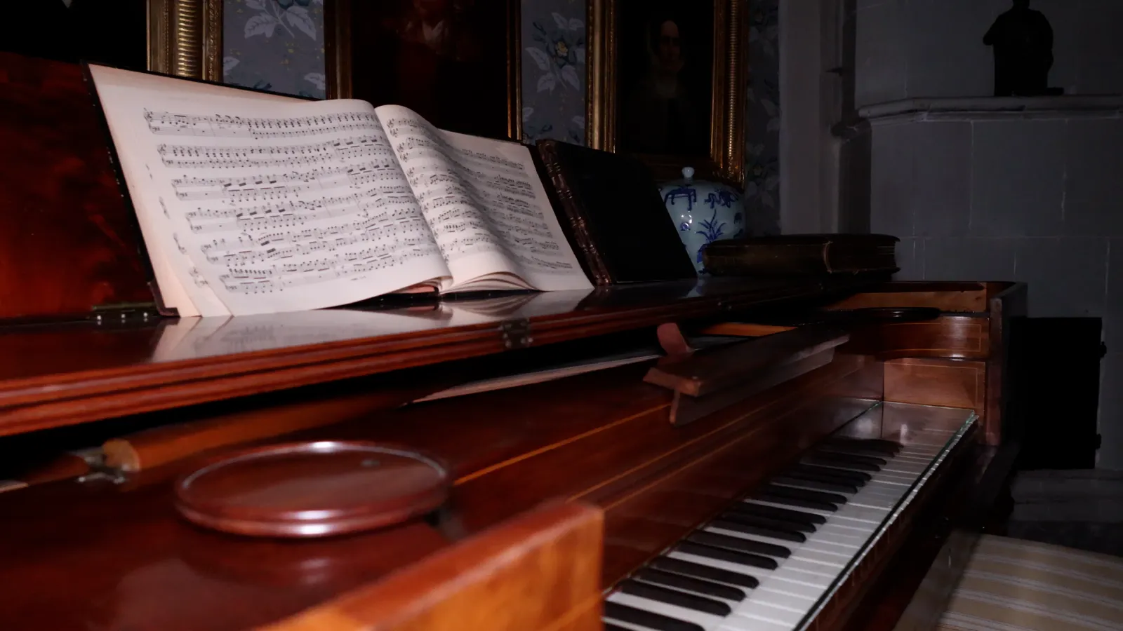 An open piano with sheet music still on the stand in a dark room of gilt picture frames