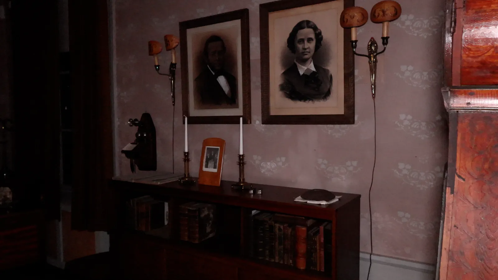 Two framed portraits of a long-dead couple hanging above a sideboard with candlesticks