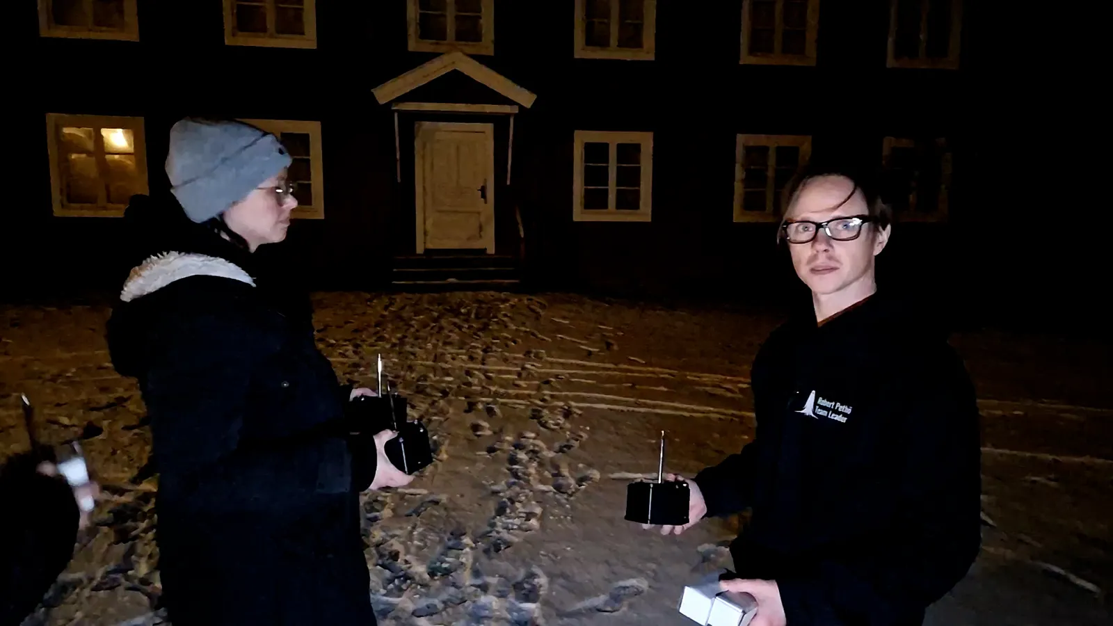 Ylva and Robert outside Gästgivars at night, each holding a sensor