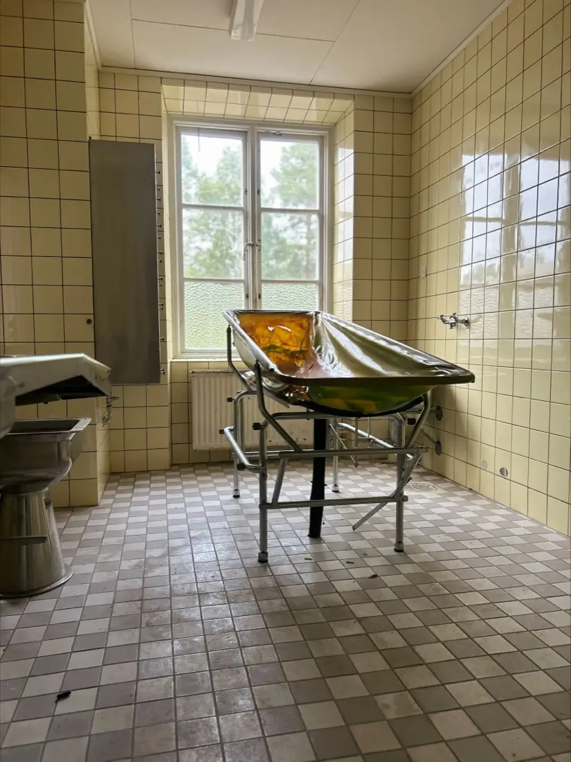 A tiled treatment room with an old bathing stretcher on a frame