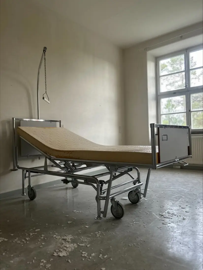 A hospital bed with an abandoned mattress in an empty patient room